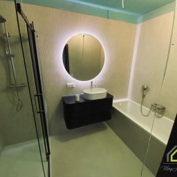 MeryArt Home - Nowoczesna łazienka z kabiną prysznicową, podwieszaną szafką z umywalką i okrągłym lustrem z podświetleniem LED. Jasne płytki na ścianach.