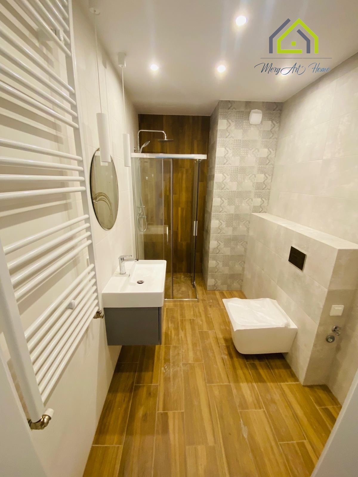 Nowoczesna łazienka po remoncie: kabina prysznicowa ze złotymi akcentami, umywalka z szafką, grzejnik drabinkowy i płytki imitujące drewno na podłodze.