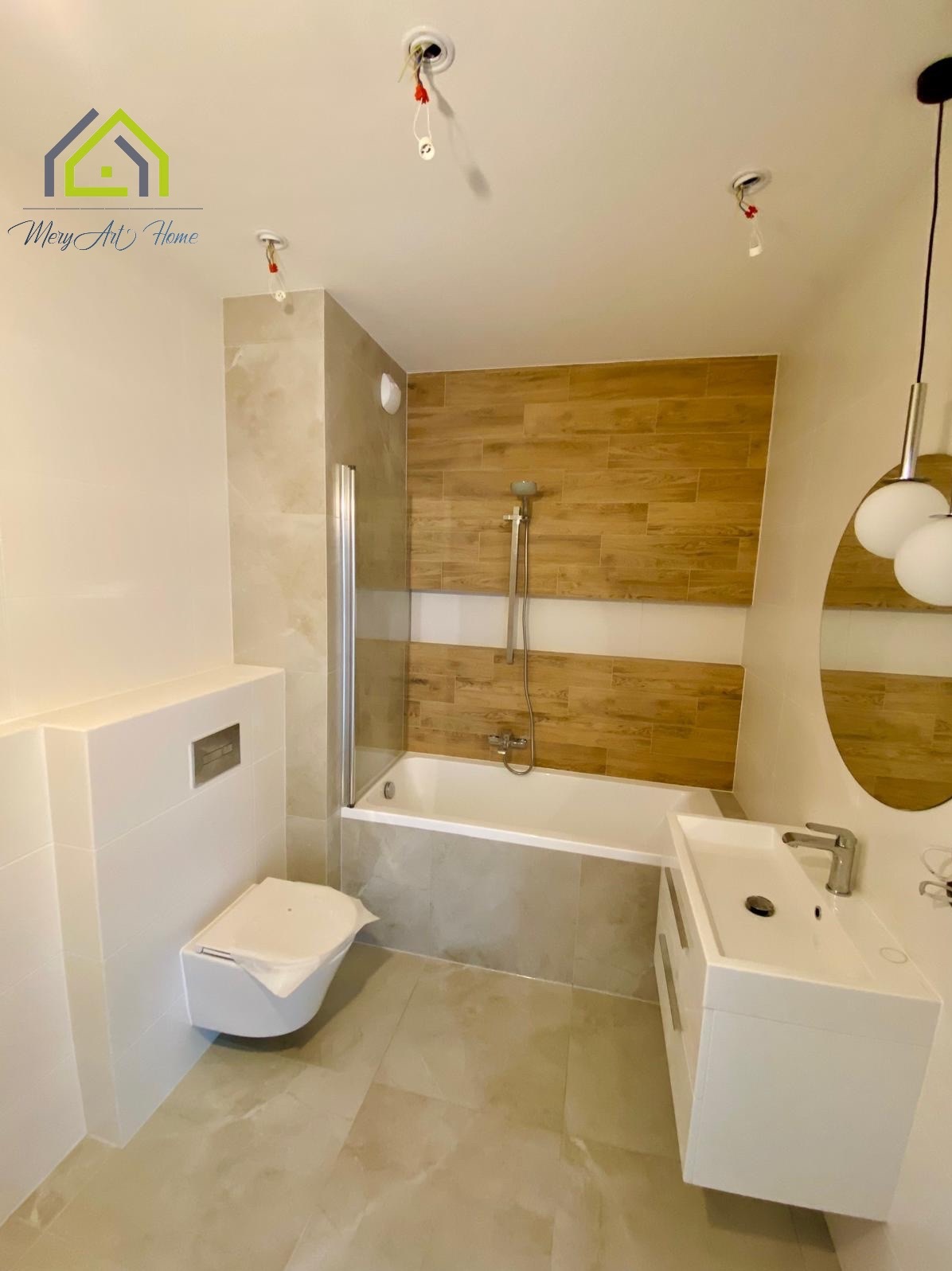 Nowoczesna łazienka po remoncie: biała armatura, drewnopodobne płytki na ścianach, kabina prysznicowa ze szklanym panelem, wisząca toaleta i umywalka z szafką.