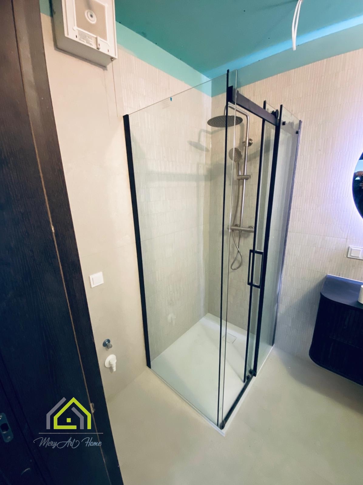 Nowoczesna kabina prysznicowa z czarnymi ramami w wyremontowanej łazience z turkusowym sufitem. Widoczna armatura i umywalka. Ujęcie z boku.