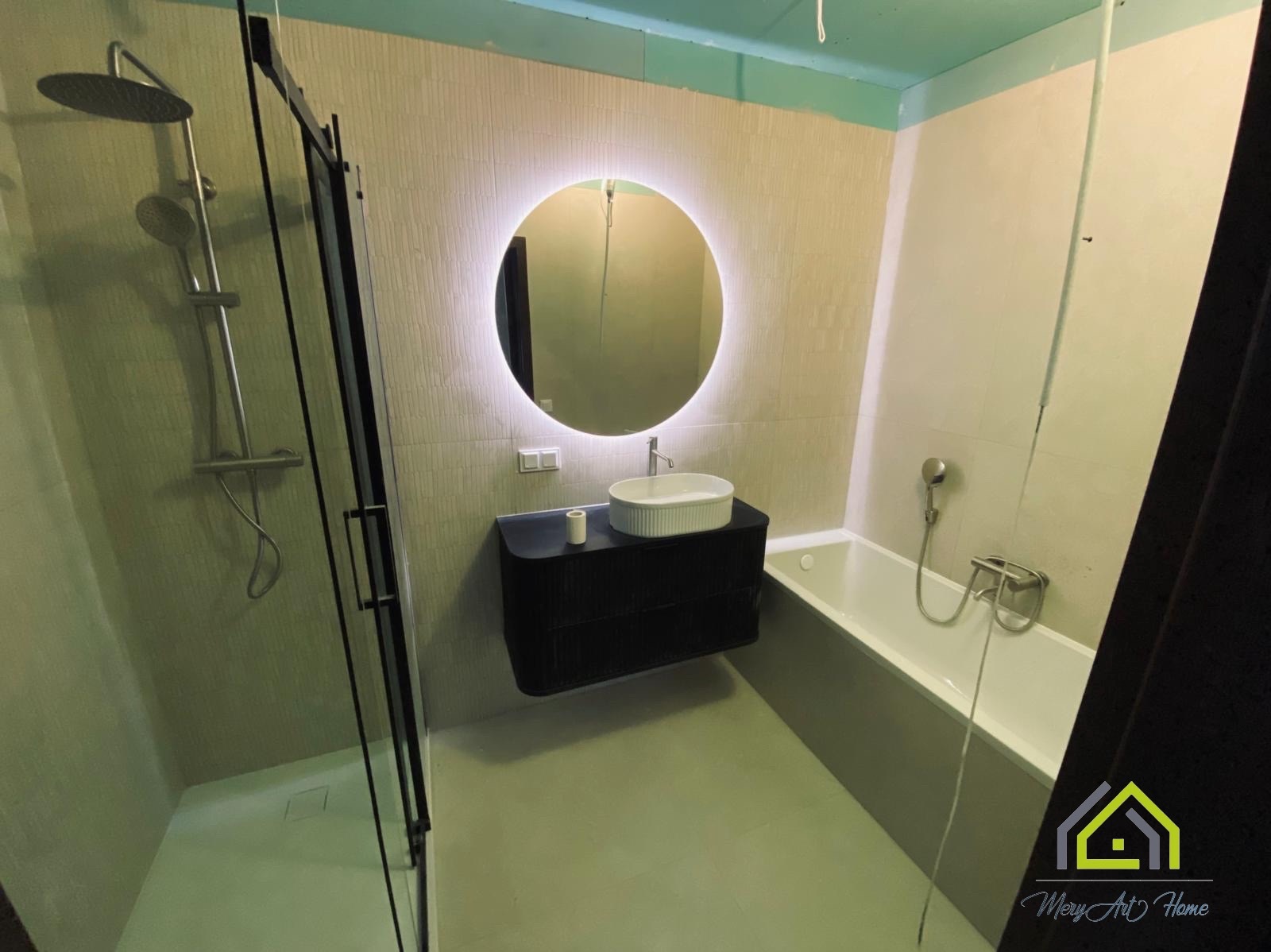 Nowoczesna łazienka z kabiną prysznicową, podwieszaną szafką z umywalką i okrągłym lustrem z podświetleniem LED. Jasne płytki na ścianach.