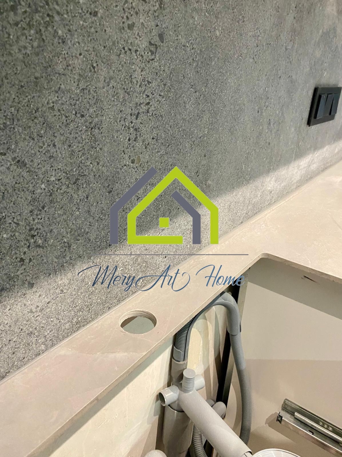 Szara ściana z gniazdkiem nad beżowym blatem z otworem i szarą instalacją hydrauliczną w wykończonej łazience.