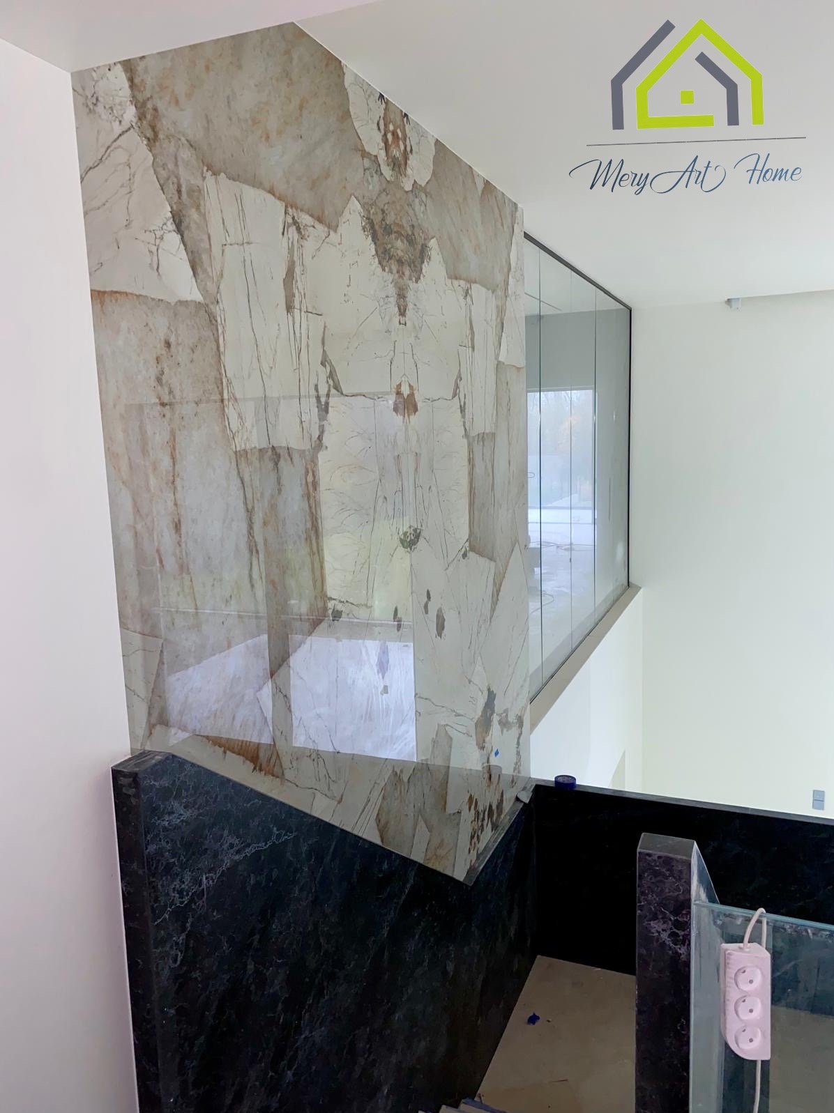 Wykończenie ściany marmurem z unikalnym wzorem i szklaną balustradą. Widok z góry na schody z ciemnego marmuru. Nowoczesne wnętrze z dbałością o detale.