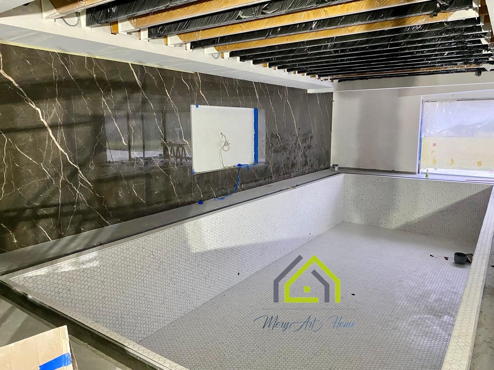 Wnętrze basenu w trakcie wykańczania: biała mozaika heksagonalna na dnie i ścianach, marmurowe płytki na ścianie, zabezpieczone elementy sufitu.