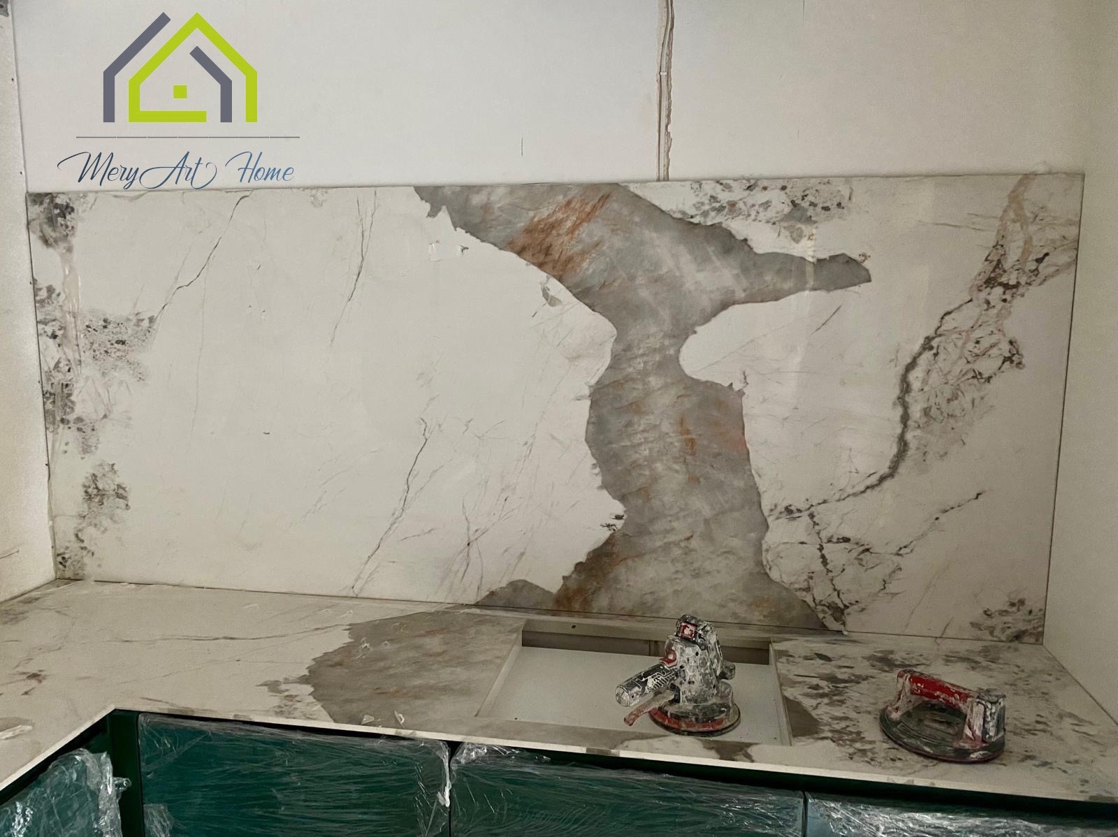 Montaż blatu kuchennego z płyty imitującej marmur, widoczne narzędzia glazurnicze i fragment szafek kuchennych zabezpieczonych folią.