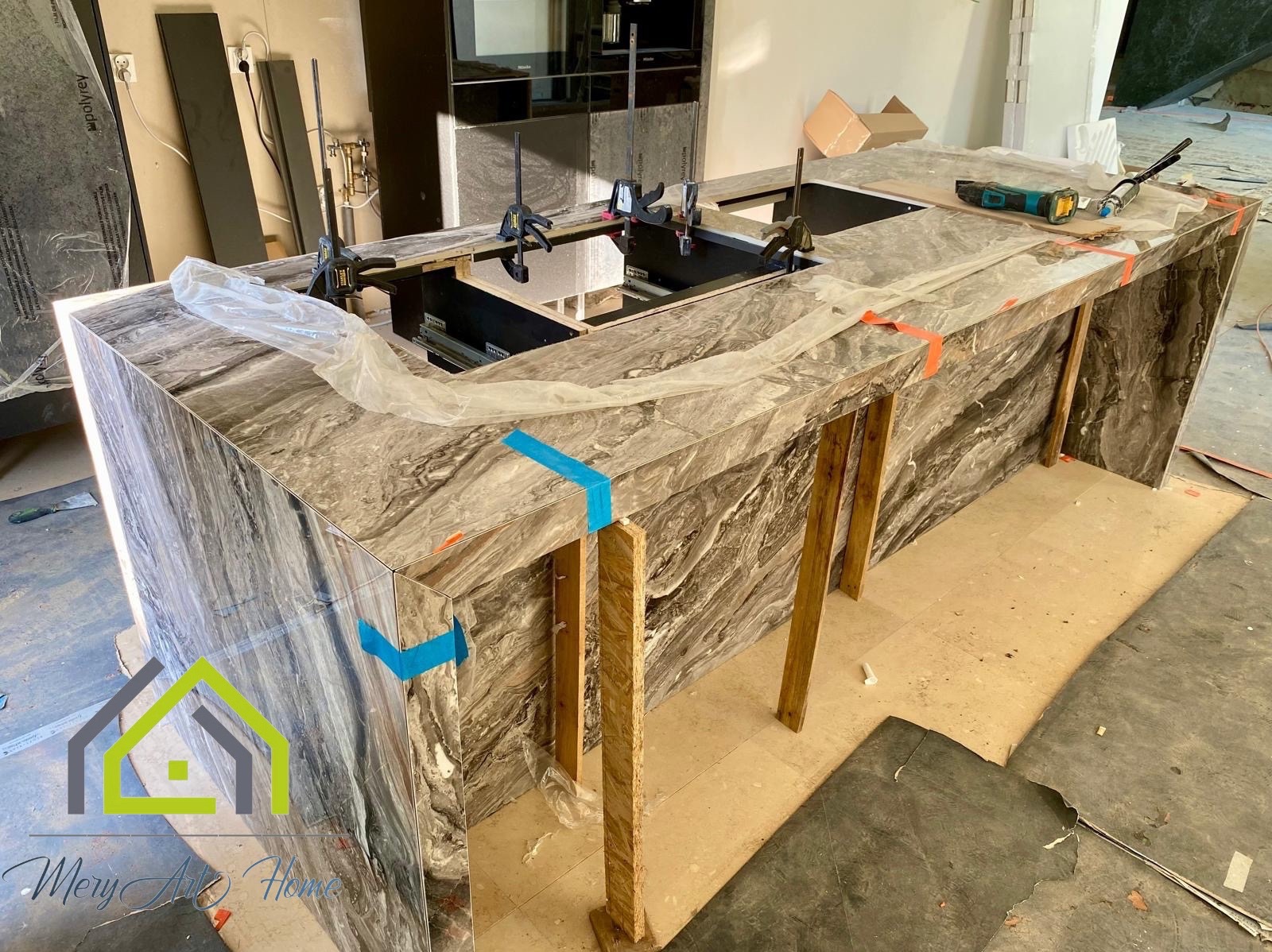 Montaż blatu kuchennego z marmuru, zabezpieczonego folią i podpartego drewnianymi elementami. Widoczne narzędzia i mocowania.