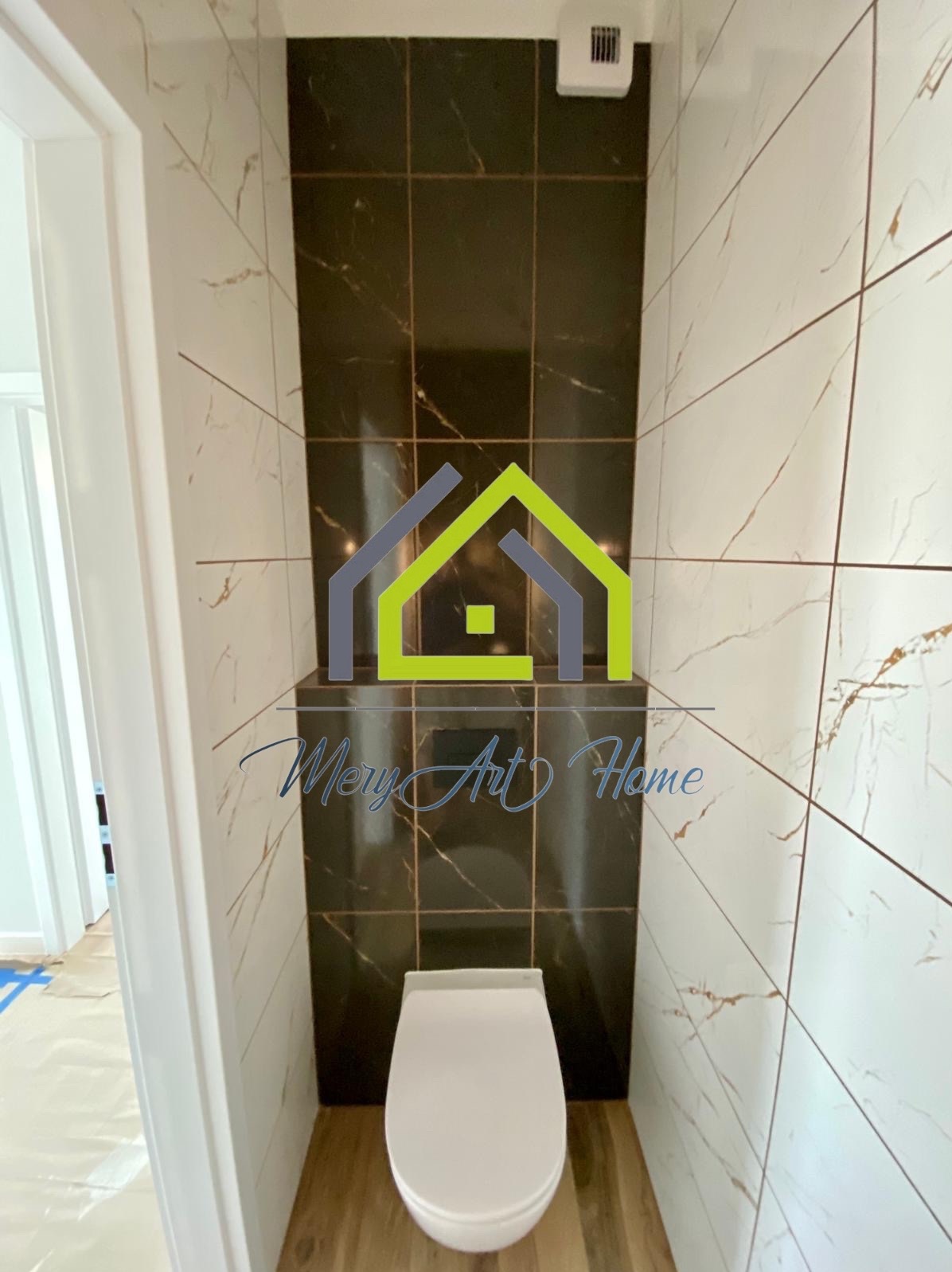 Wykończona toaleta z białą miską ustępową i brązowo-białymi płytkami imitującymi marmur na ścianach. Widok z perspektywy wejścia do pomieszczenia.