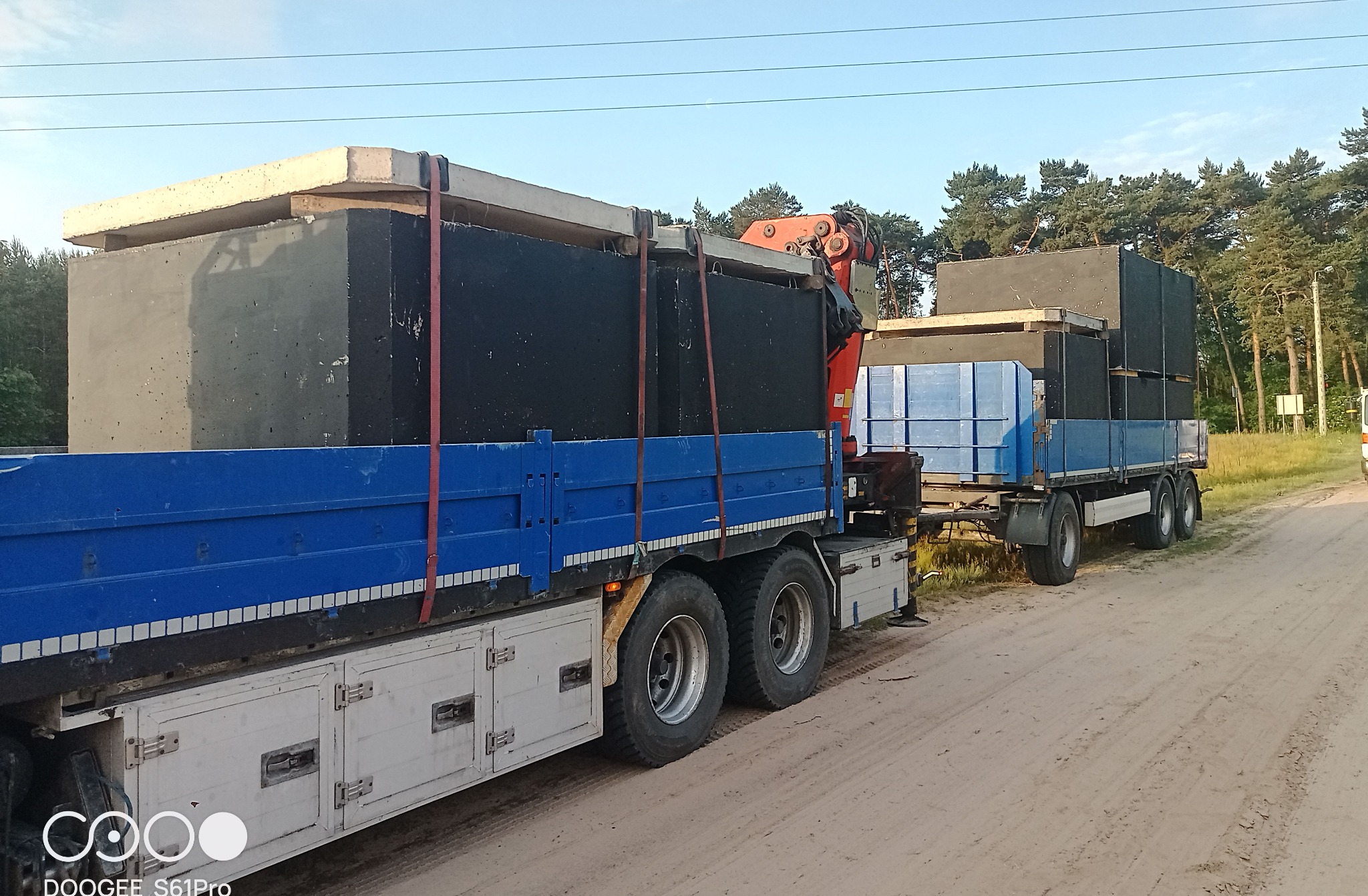 Transport betonowych szamb na lawecie z dźwigiem HDS, widok z boku na leśnej drodze gruntowej.