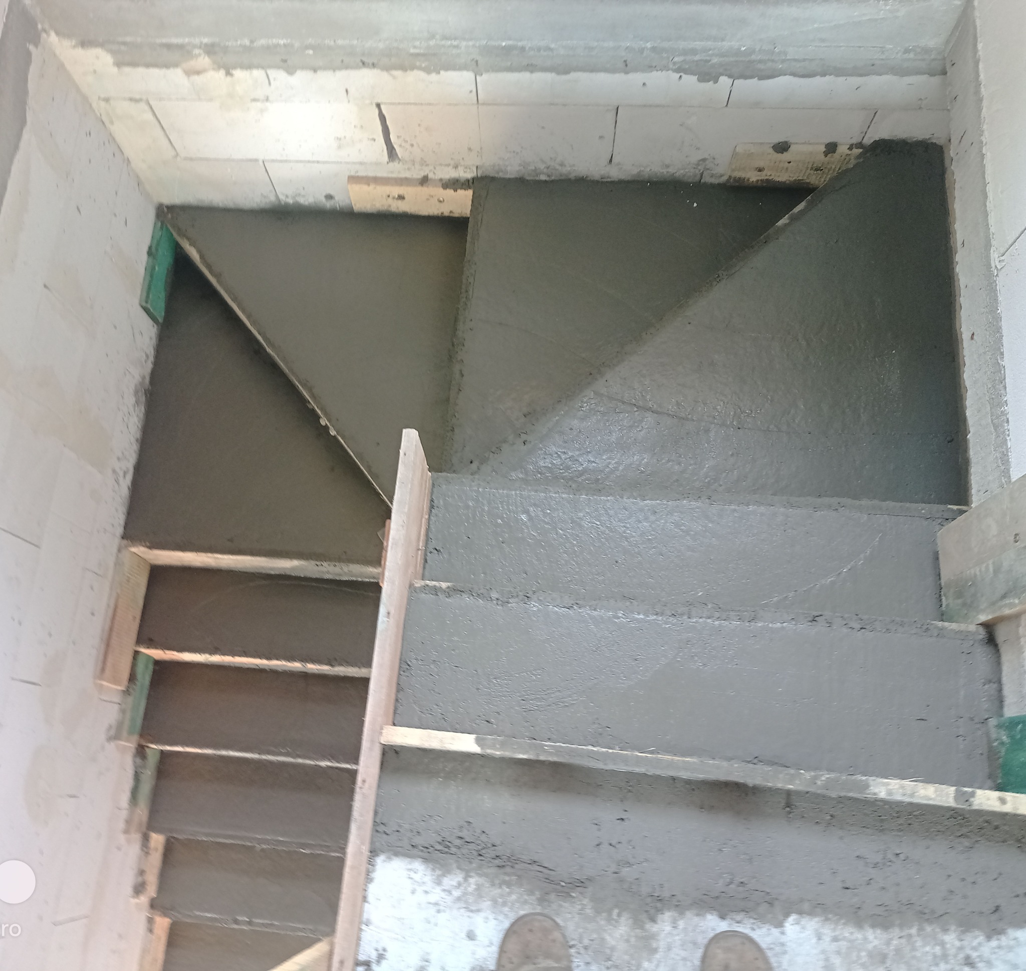 Wylane betonowe schody w surowym stanie, z widocznym szalunkiem i elementami konstrukcyjnymi. Kąt ujęcia z góry podkreśla spiralny kształt.