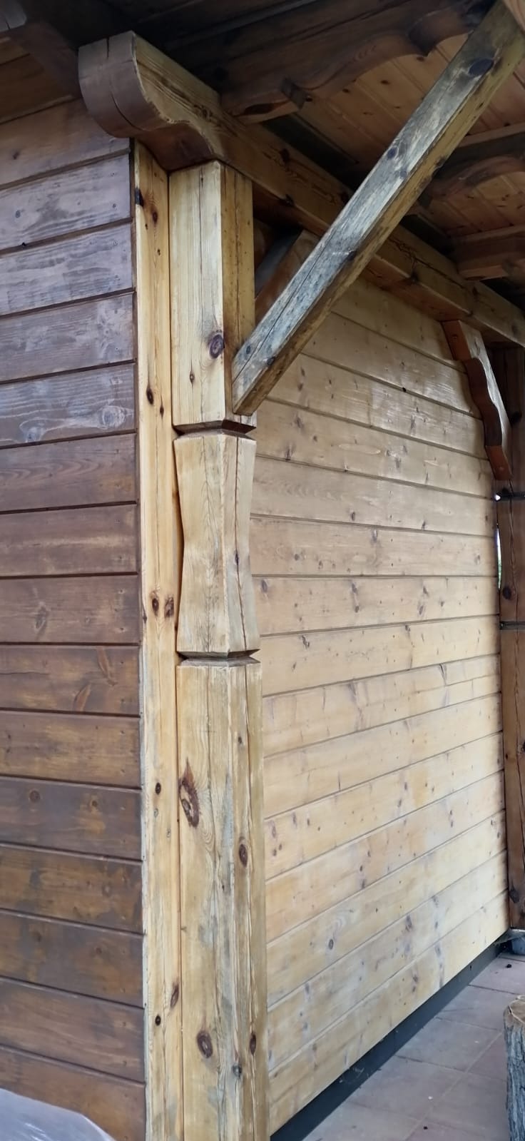 Fragment drewnianej konstrukcji z elementami bejcowanymi i surowymi. Widoczne połączenia belek i desek, detale obróbki drewna w stylu rustykalnym.