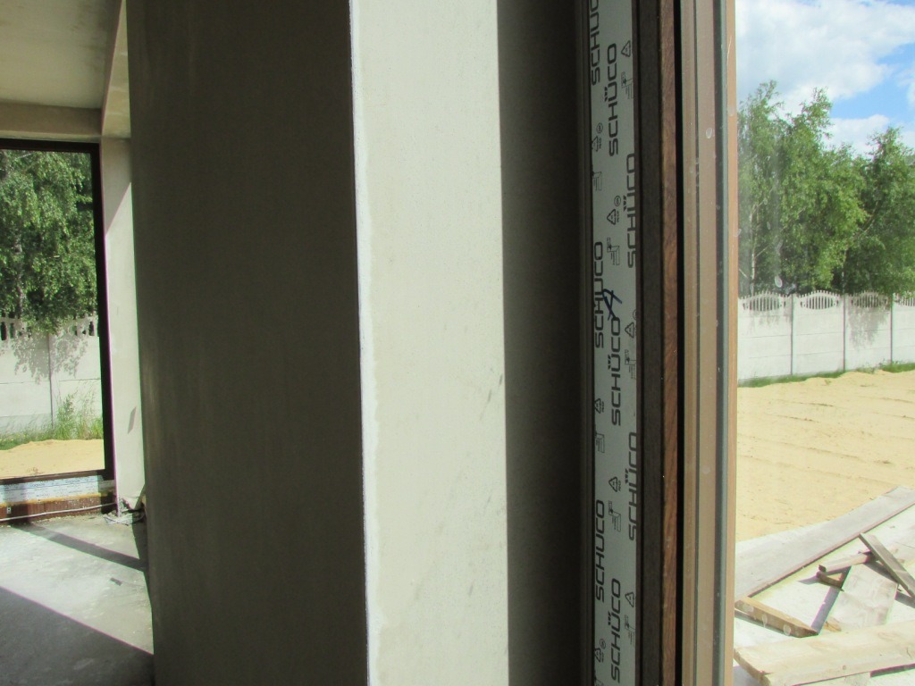 Świeżo położony tynk na ścianie wewnętrznej budynku w stanie surowym otwartym, widok z okna na zewnątrz.