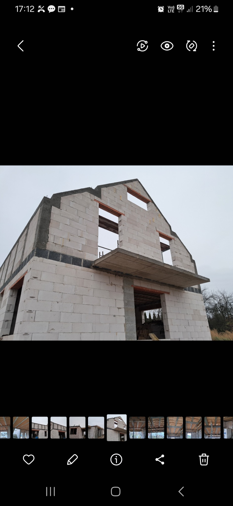 Surowy stan domu z białych bloczków, widoczne otwory okienne i drzwiowe, strop nad wejściem. Budynek w trakcie wznoszenia, szary dzień.