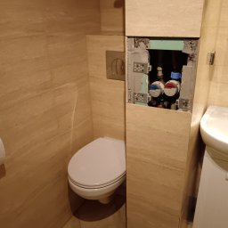 Monolit - Łazienka w trakcie remontu: widoczny sedes i zabudowa z odkrytymi zaworami wody, płytki imitujące marmur na ścianach i podłodze, umywalka z szafką obok.