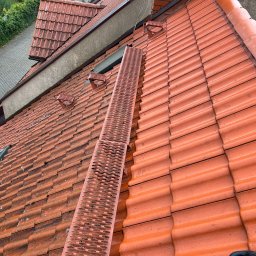 Teamsters - Czerwona dachówka z ławą kominiarską na dachu w Szczecinie. Widoczne okno dachowe i fragment chodnika z zielenią w tle. Ujęcie z góry.