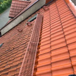 Czerwona dachówka z ławą kominiarską na dachu w Szczecinie. Widoczne okno dachowe i fragment chodnika z zielenią w tle. Ujęcie z góry.