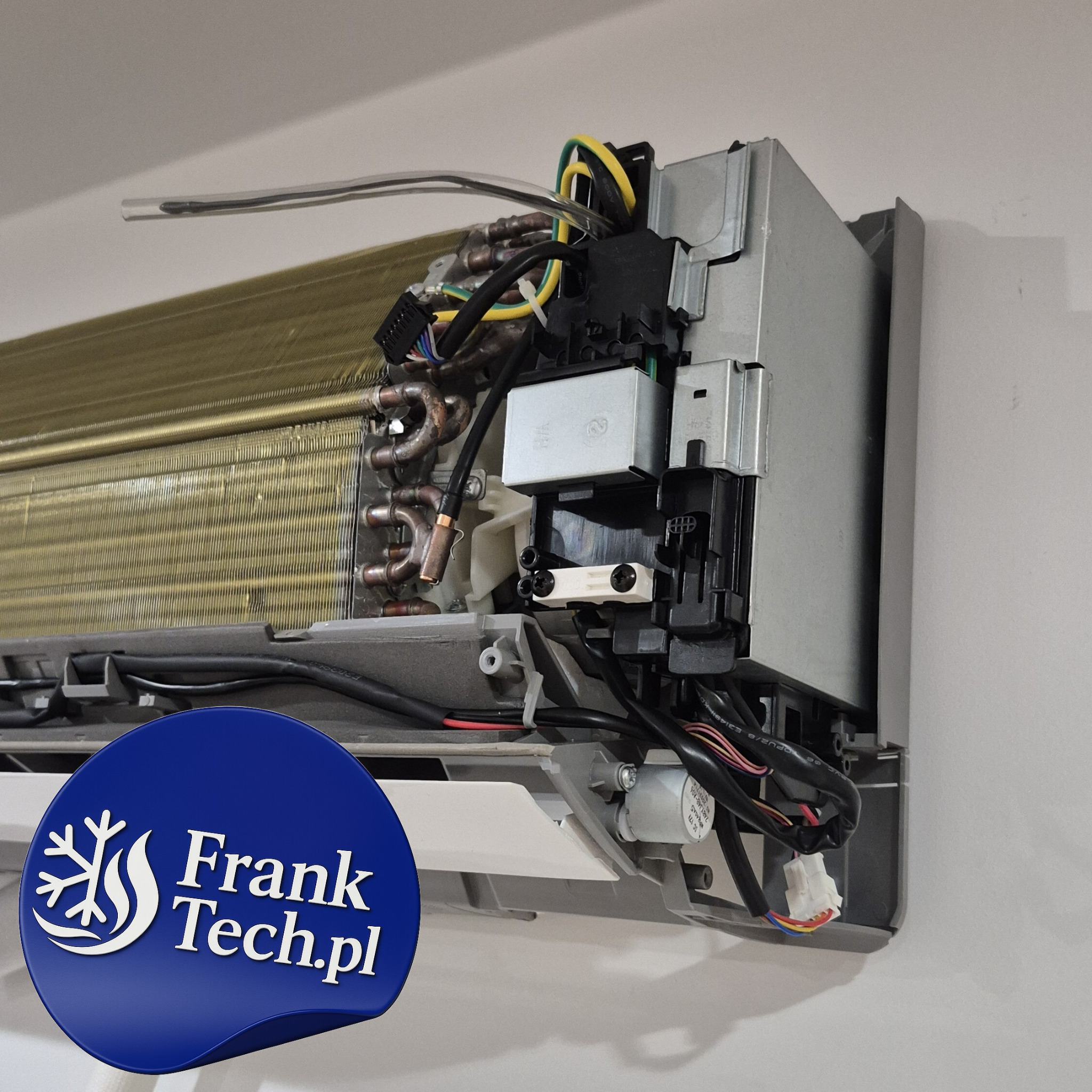 Rozłożona jednostka wewnętrzna klimatyzacji na ścianie, widoczne elementy instalacji i okablowanie. Na dole naklejka z logo firmy Frank Tech.pl.