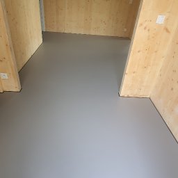 MARMOR Mikrocement4you - Szara, gładka posadzka w pokoju wykończonym drewnianą boazerią. Na ścianie wisi obraz. Nowoczesne wnętrze z minimalistycznym designem.