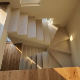 Minimalistyczne schody z mikrocementu, widok z góry, naturalne światło podkreśla fakturę. Drewniana podłoga i stopnie tworzą harmonijną całość.