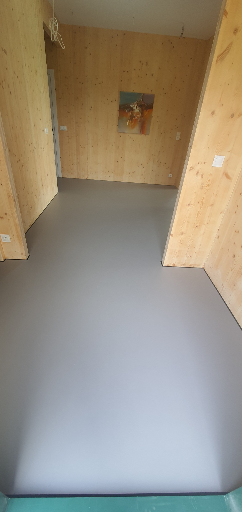 Szara, gładka posadzka w pokoju wykończonym drewnianą boazerią. Na ścianie wisi obraz. Nowoczesne wnętrze z minimalistycznym designem.