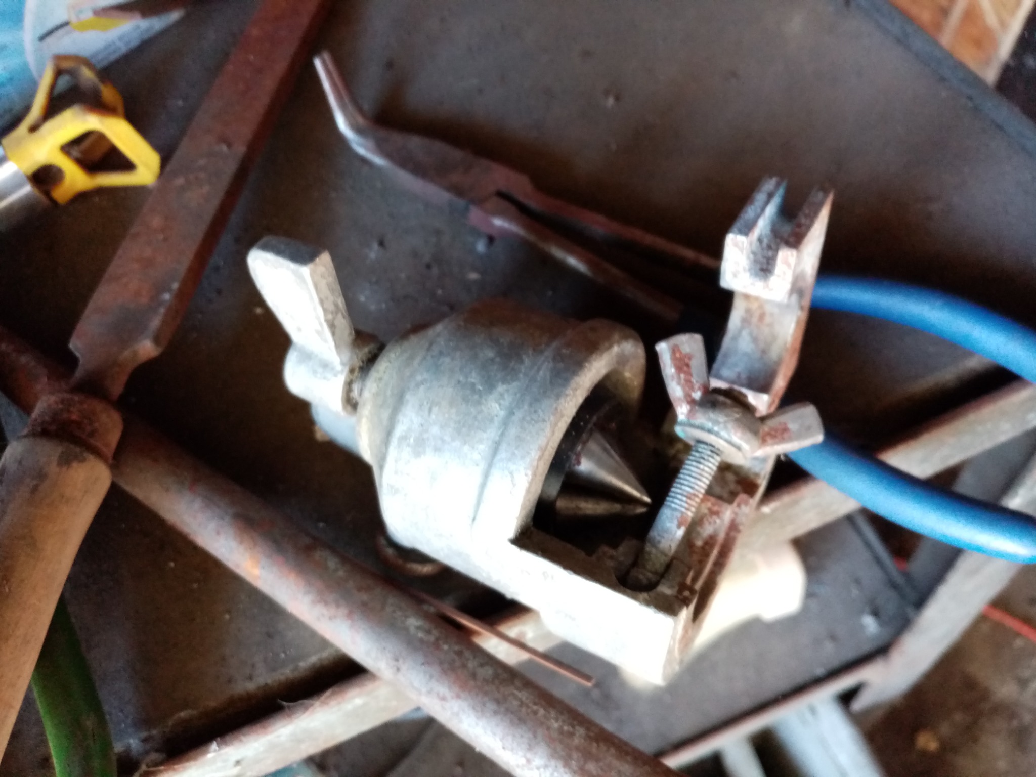 Warsztat ślusarski: narzędzia, w tym rozwiertak stożkowy, szczypce z niebieskimi uchwytami i pilnik z drewnianą rączką, ułożone na brudnym, metalowym stole.