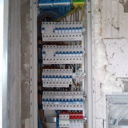 Usługi elektryczne - Rozdzielnica elektryczna Hager z zainstalowanymi bezpiecznikami i przewodami, zamontowana na ścianie z pustaków, zabezpieczona pianką montażową.