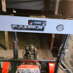 Usługi elektryczne - Wnętrze kabiny traktora z zamontowanym radiem samochodowym i głośnikami w szarej obudowie podsufitowej. Widok z perspektywy kierowcy na deskę rozdzielczą i silnik.