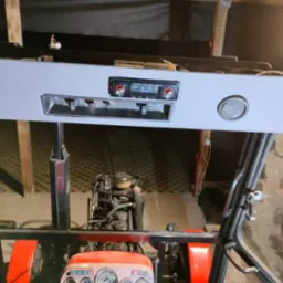 Wnętrze kabiny traktora z zamontowanym radiem samochodowym i głośnikami w szarej obudowie podsufitowej. Widok z perspektywy kierowcy na deskę rozdzielczą i silnik.