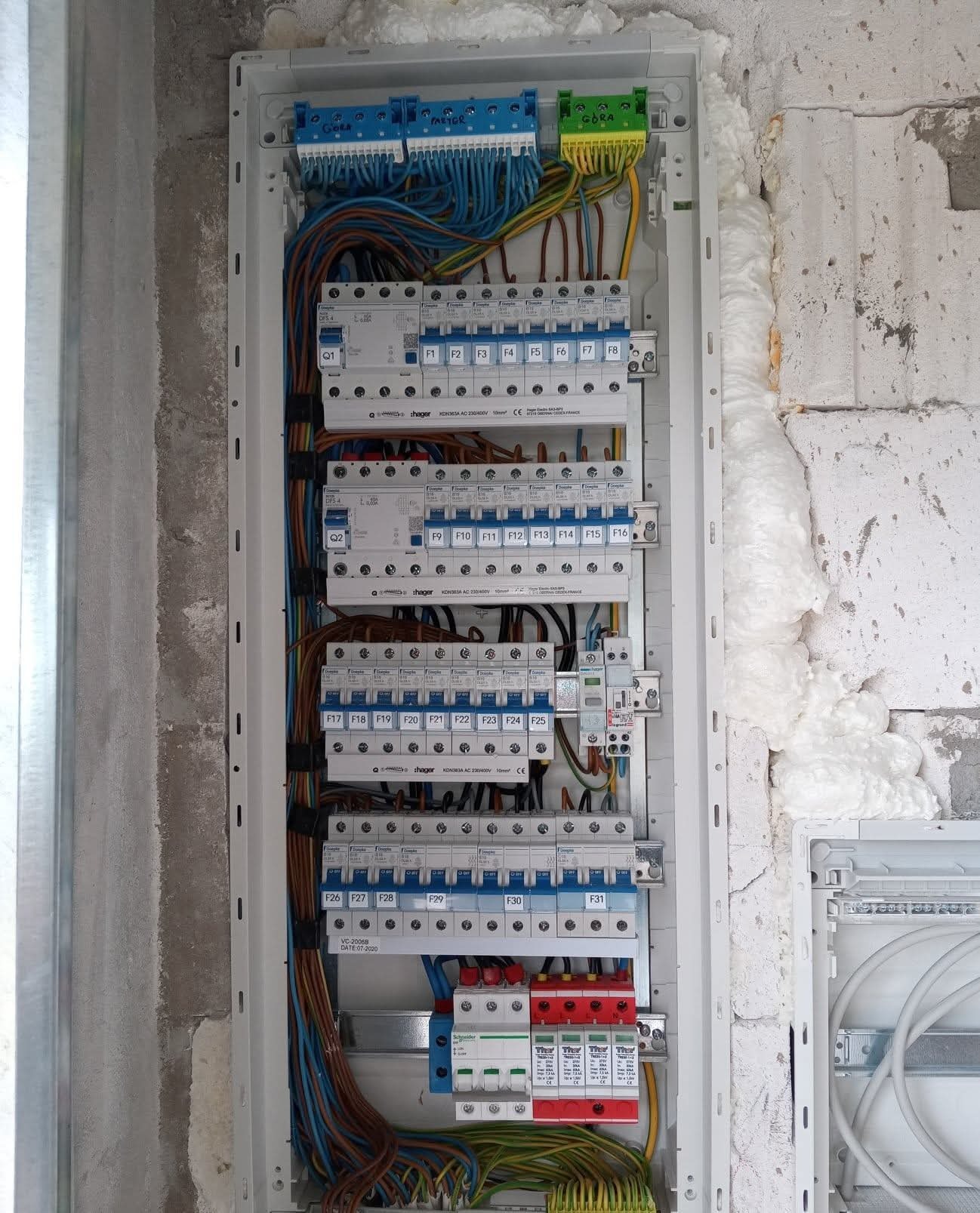 Rozdzielnica elektryczna Hager z zainstalowanymi bezpiecznikami i przewodami, zamontowana na ścianie z pustaków, zabezpieczona pianką montażową.