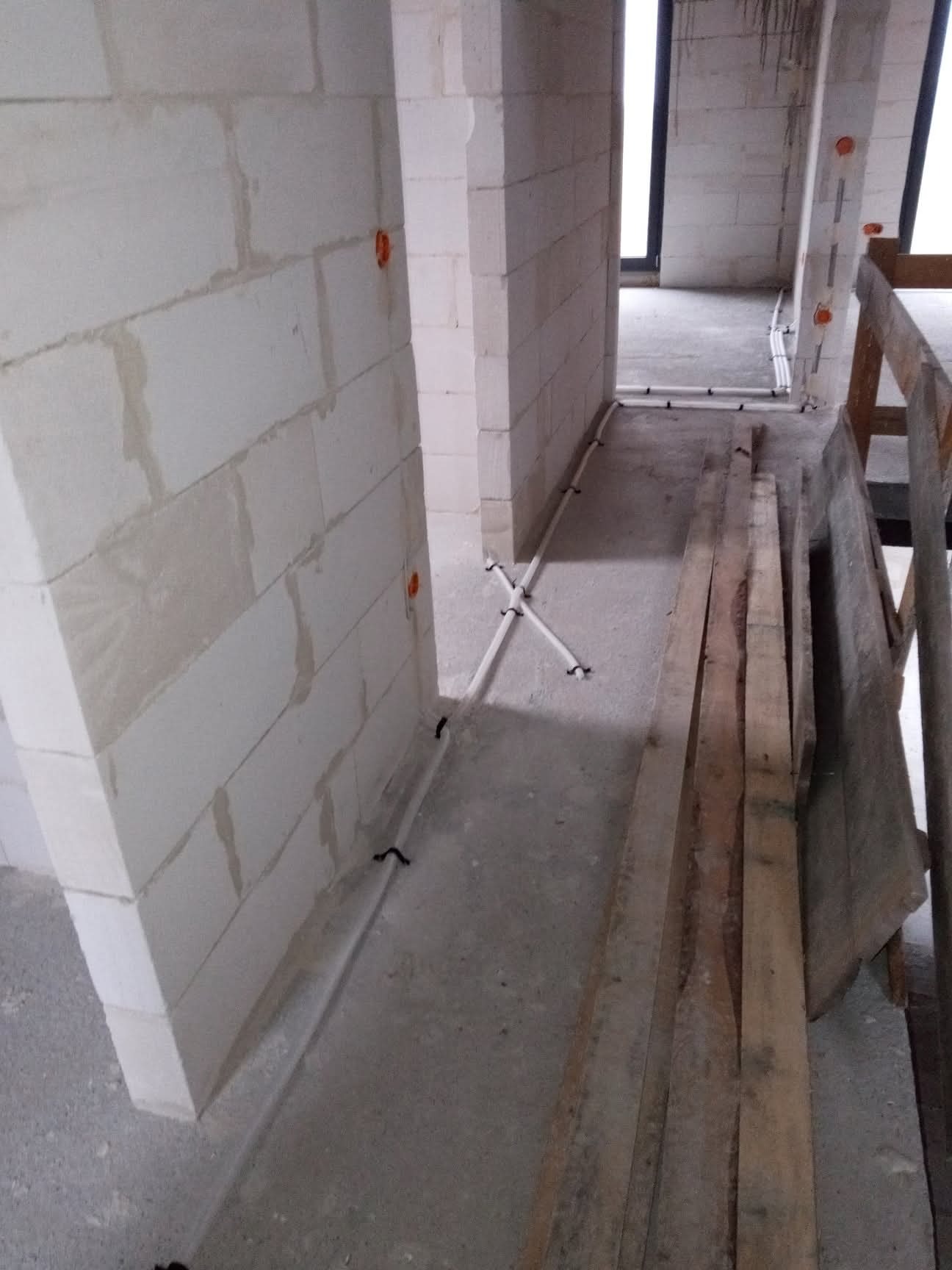 Wnętrze w trakcie budowy z instalacją elektryczną w rurkach PVC, widoczne puszki elektryczne w ścianach z betonu komórkowego i fragment rusztowania z desek.