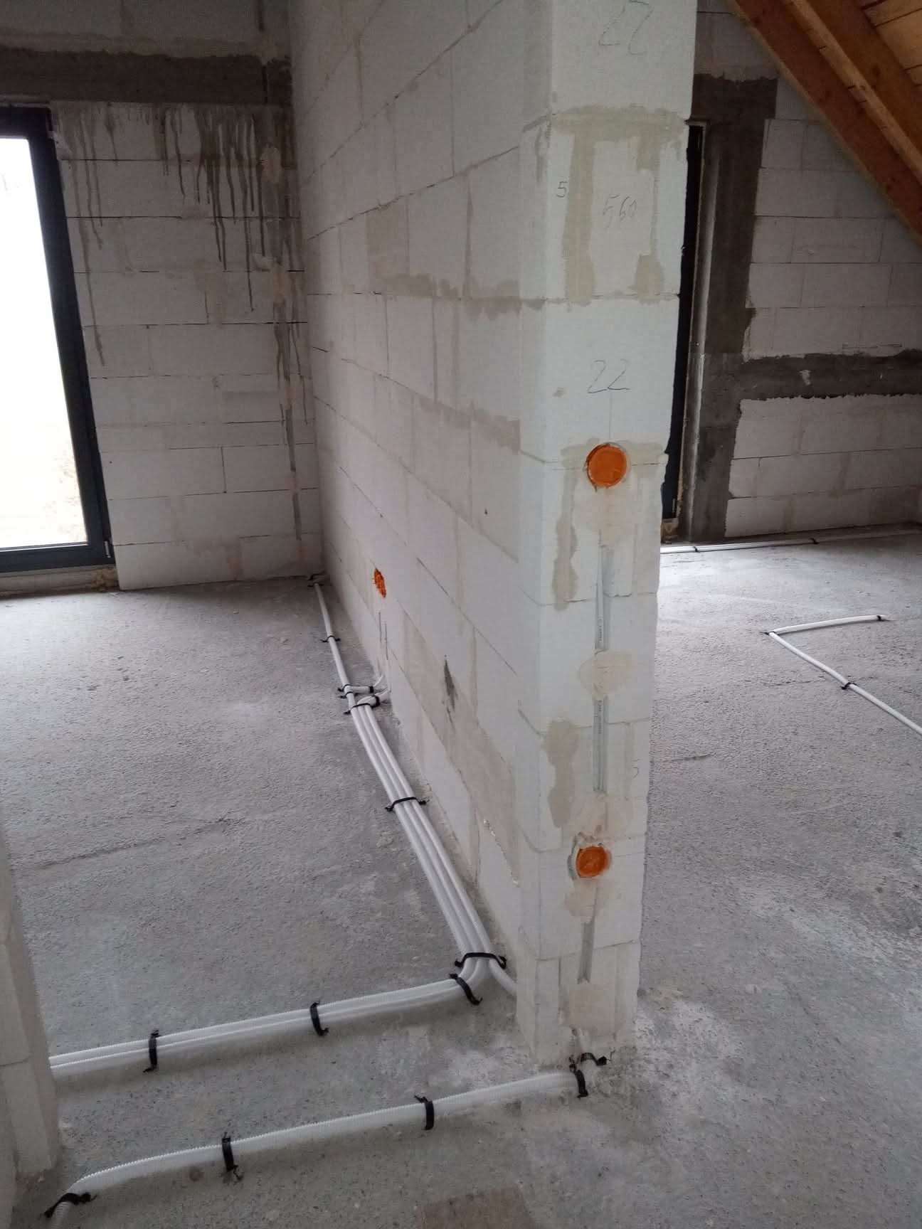 Wewnętrzne instalacje elektryczne w rurach PCV, prowadzone po ścianie z betonu komórkowego w surowym stanie. Widoczne puszki instalacyjne w ścianie.