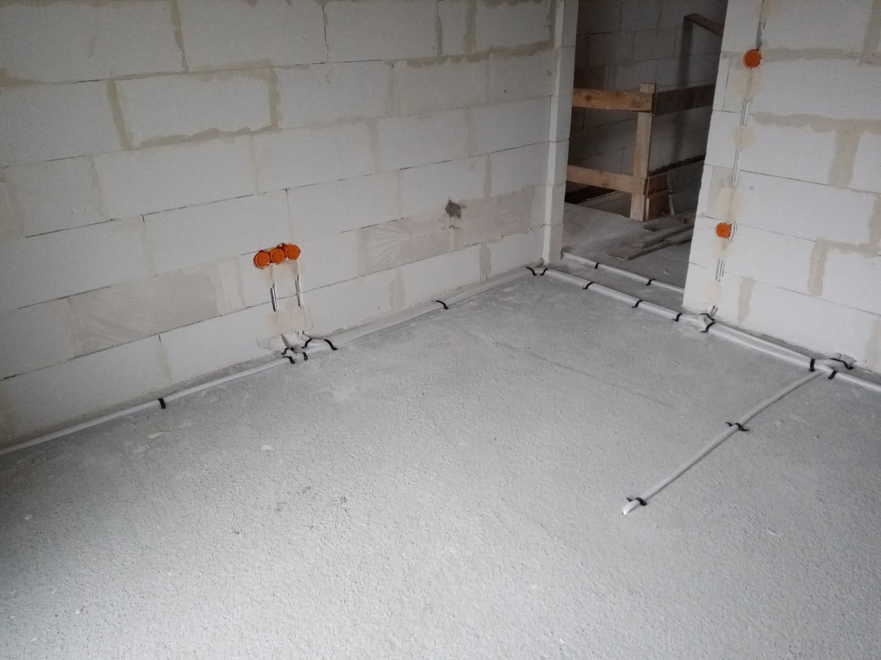 Instalacja elektryczna podtynkowa w nowym budynku z bloczków, rury prowadzone po podłodze, pomarańczowe puszki elektryczne w ścianach. Widoczne mocowania kabli.