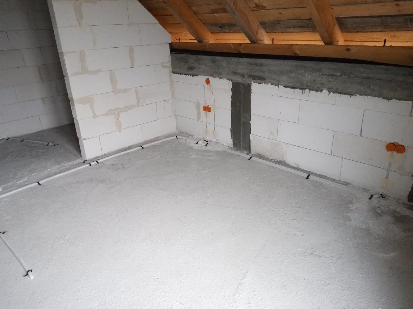 Surowy stan poddasza z instalacją elektryczną w peszlach, widoczne puszki instalacyjne w ścianie z betonu komórkowego, przygotowane do dalszych prac wykończeniowych.