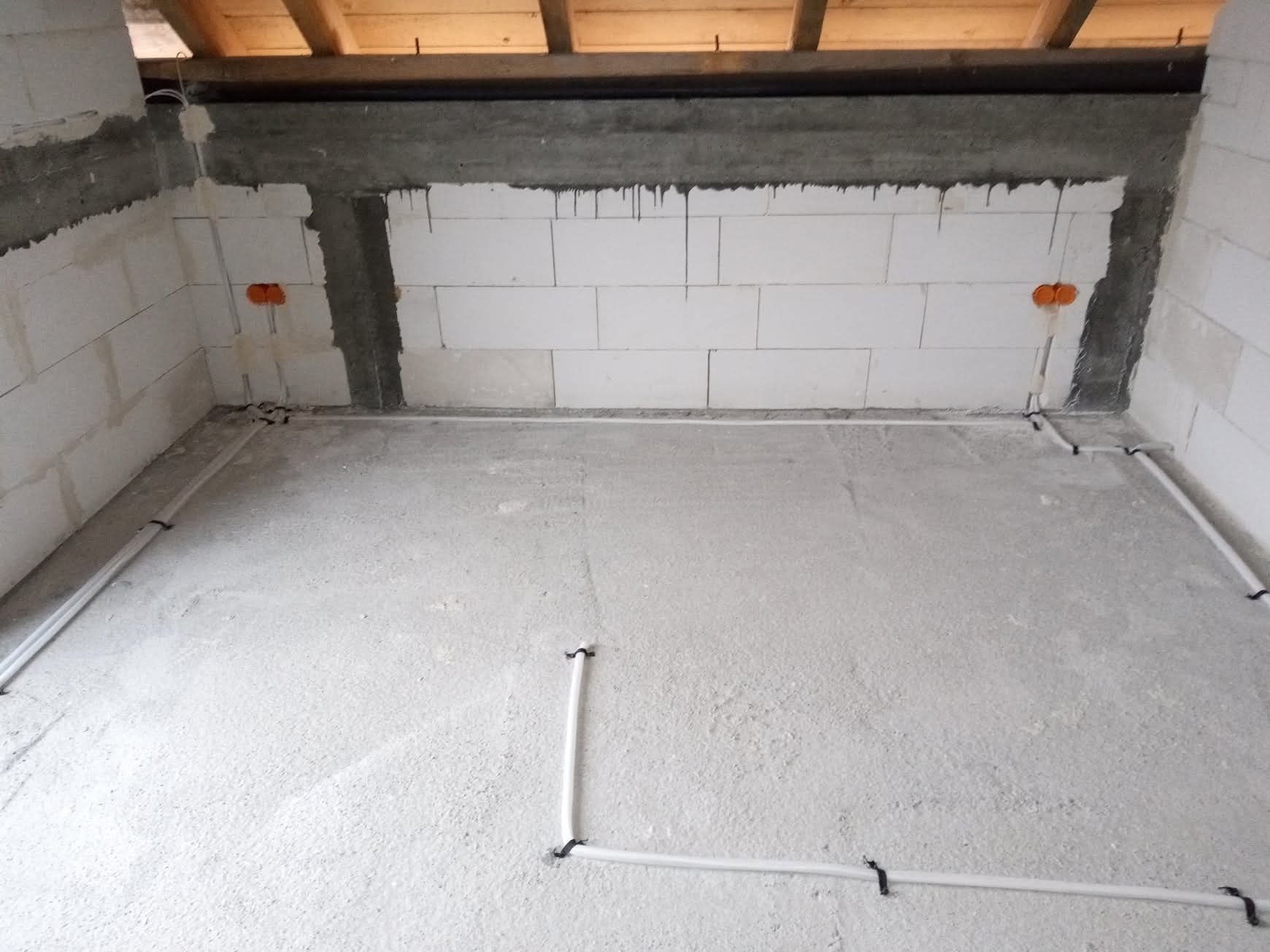 Surowy stan wnętrza z instalacją elektryczną w peszlach na podłodze, widoczne puszki elektryczne w ścianach z betonu komórkowego i drewniany strop.