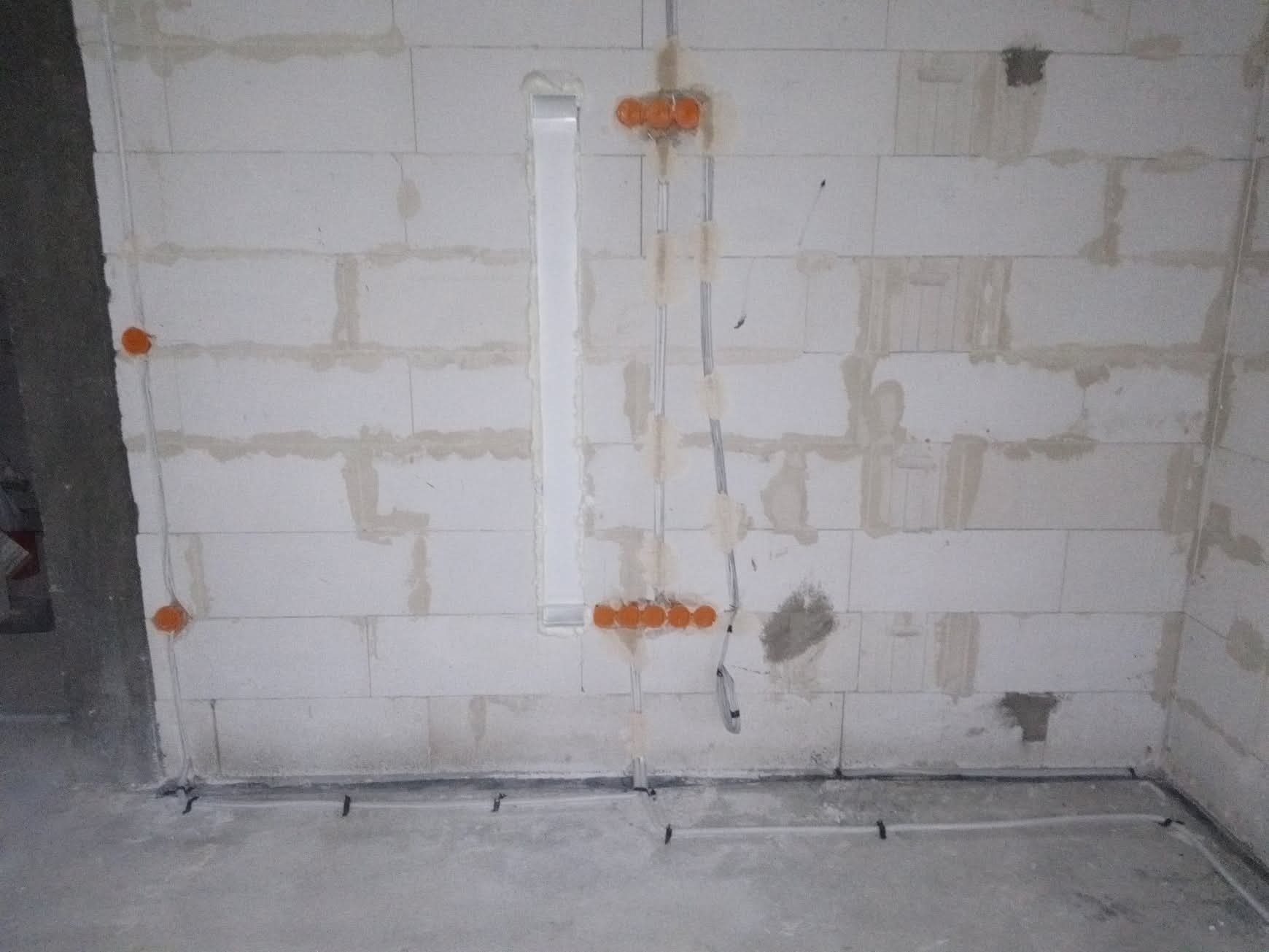Instalacja elektryczna w surowym wnętrzu w Niepoczołowicach: pomarańczowe puszki, kable prowadzone po ścianie z bloczków i w podłodze. Wnętrze w stanie deweloperskim.
