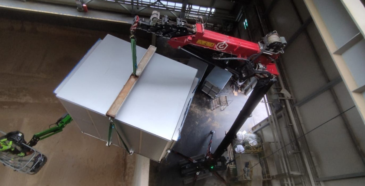 Montaż modułowej konstrukcji stalowej na hali przemysłowej za pomocą dźwigu i podnośnika koszowego. Widoczne elementy mocujące i pracownicy w kaskach.