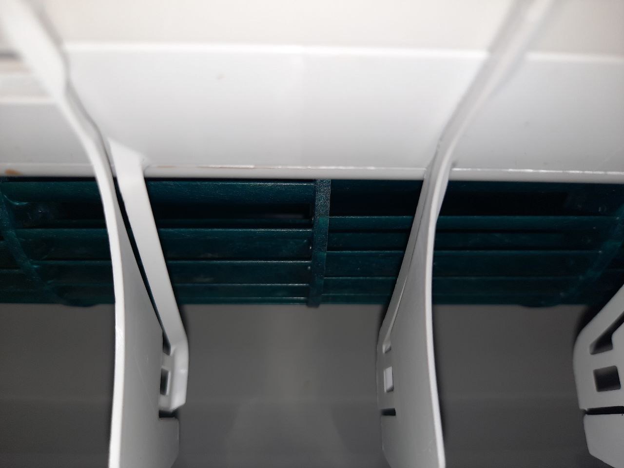 Wnętrze klimatyzatora z widocznymi, zielonymi lamelami parownika, sfotografowane z bliska pod nietypowym kątem.