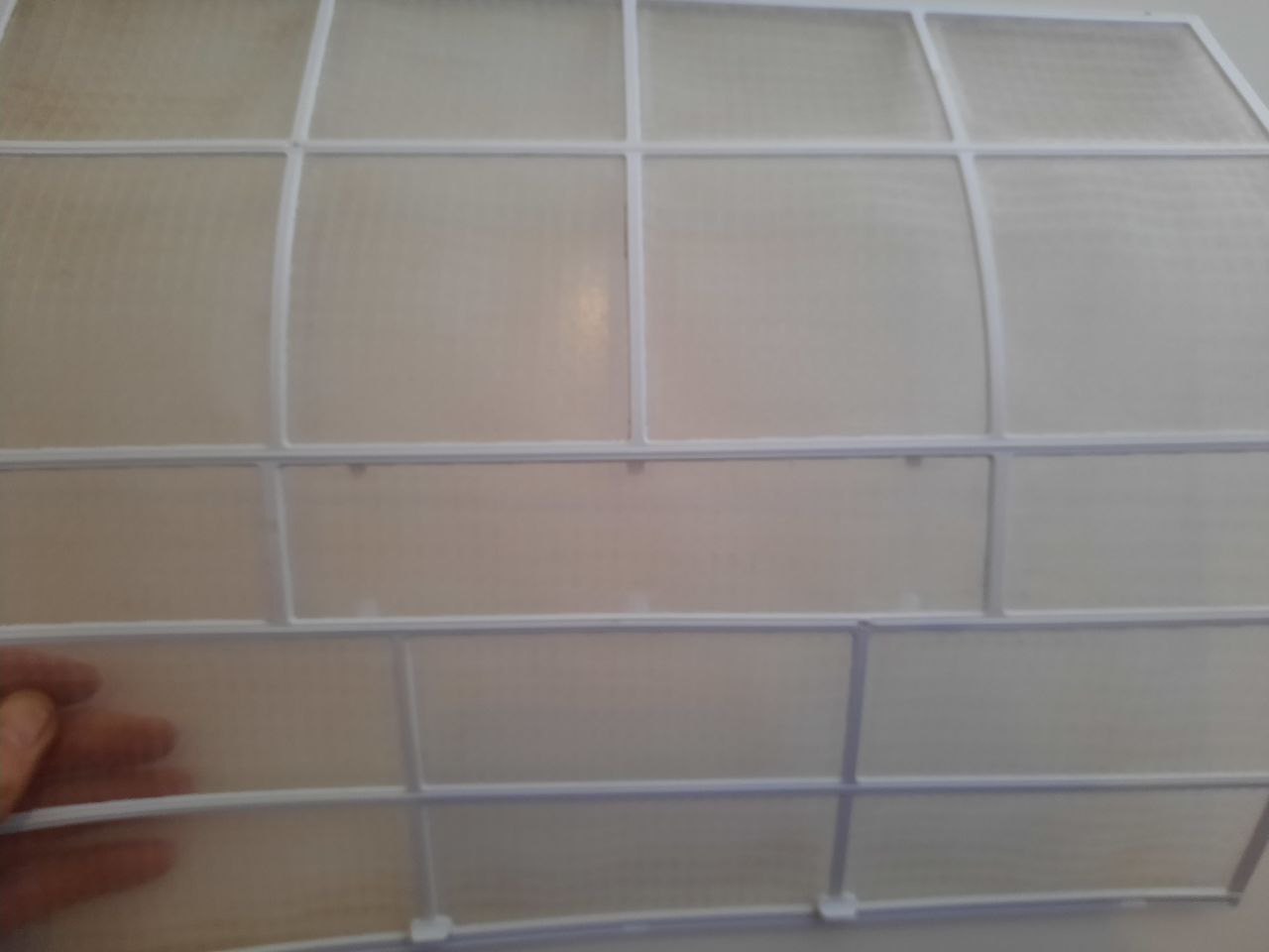 Brudny, wyjęty filtr klimatyzacji z widocznymi zabrudzeniami i siatką. Dłoń w lewym dolnym rogu trzyma filtr. Potrzeba czyszczenia.