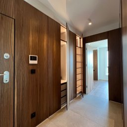 BluMeble - Nowoczesny hol z zabudową z forniru orzechowego: drzwi wejściowe, szafa wnękowa z oświetleniem LED, wideodomofon. Podłoga z płytek imitujących kamień.