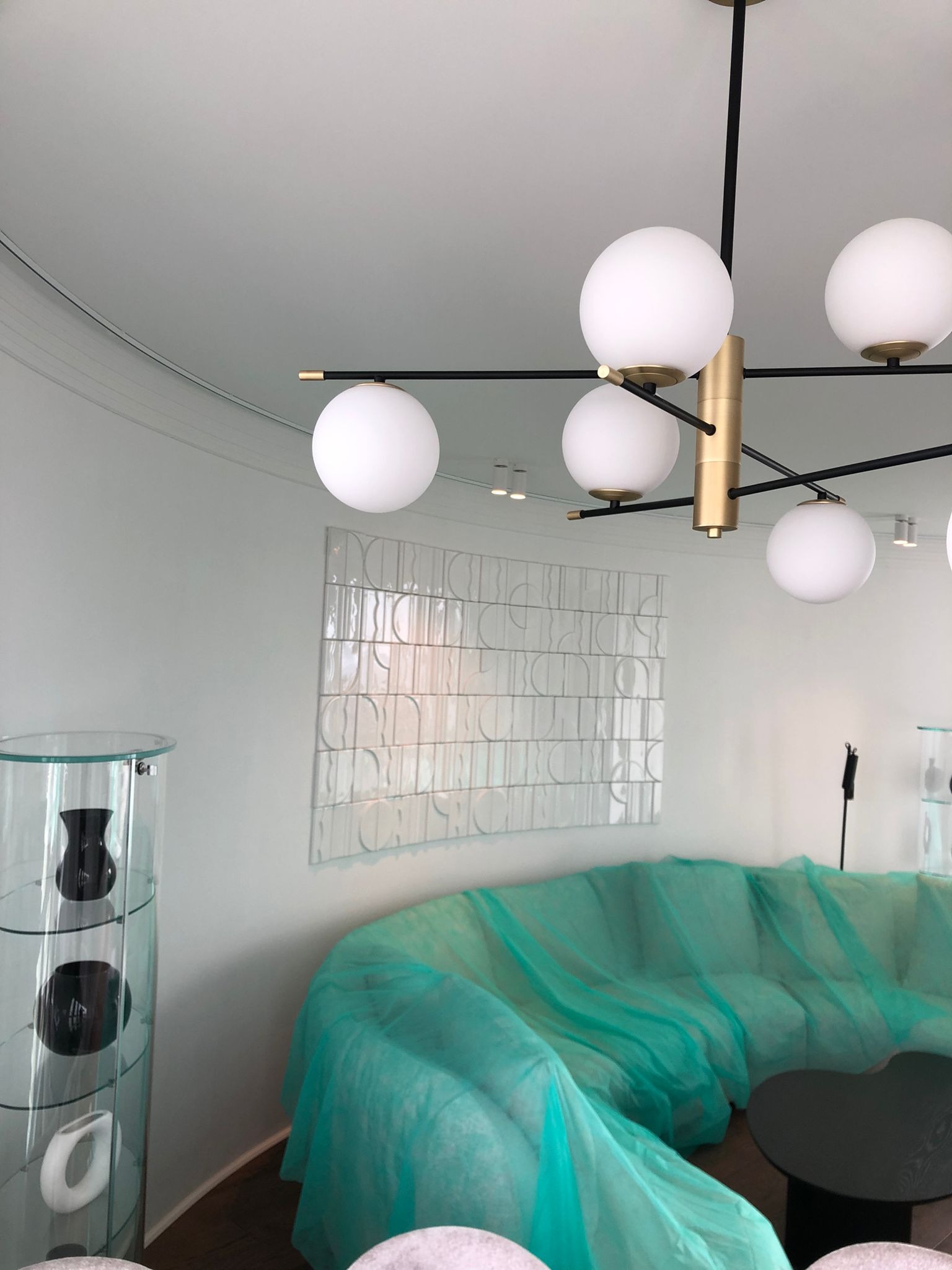 Nowoczesne wnętrze w trakcie wykończenia: sofa zabezpieczona folią, dekoracyjna ściana z płytek i designerska lampa sufitowa z kulistymi kloszami.