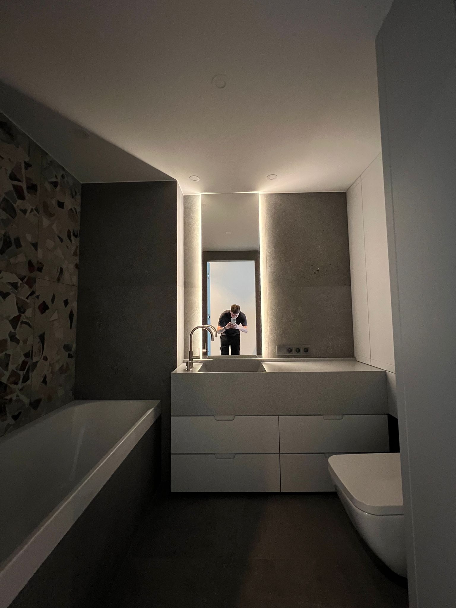 Nowoczesna łazienka z umywalką wpuszczaną w blat z szufladami, podświetlanym lustrem i płytkami mozaikowymi. Minimalistyczny design, stonowana kolorystyka.