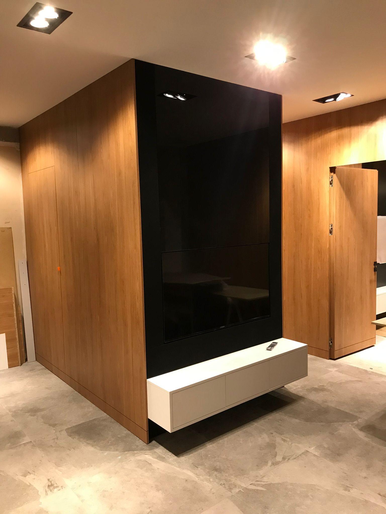 Nowoczesna zabudowa TV z drewnianymi szafami po bokach, białą szafką RTV i czarnym panelem. Minimalistyczny design z oświetleniem punktowym.