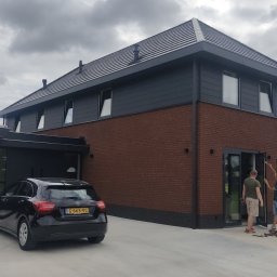 ALVECO Paweł Kępczyński - Nowoczesny dom z ciemną stolarką okienną i przesuwnymi drzwiami tarasowymi. Dwóch monterów przy pracy, narzędzia na zewnątrz. Elegancki design.