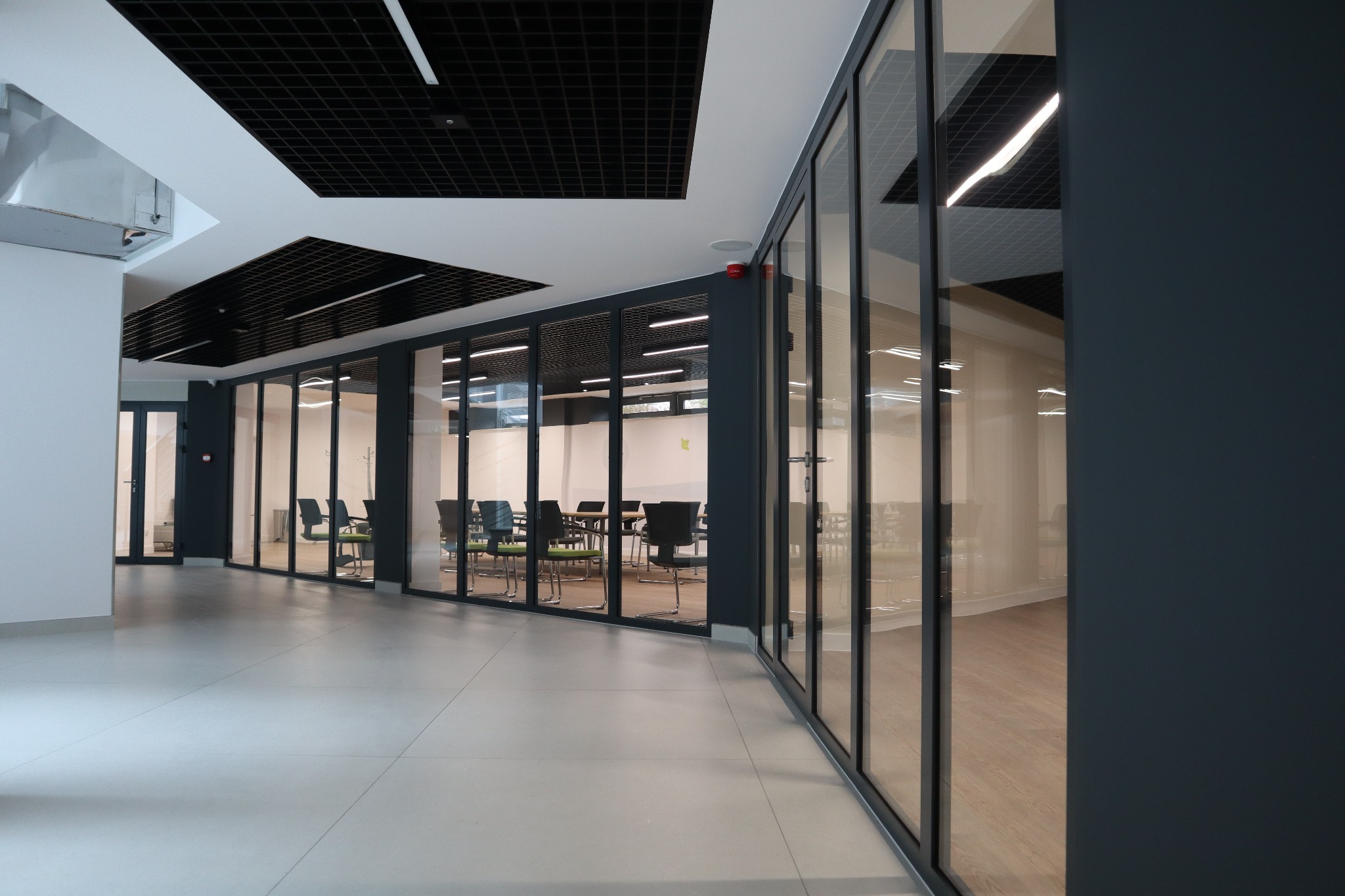 Nowoczesne, przeszklone ściany działowe z ciemnymi ramami w biurze. Widok na sale konferencyjne z krzesłami i stołami. Minimalistyczny design wnętrza.