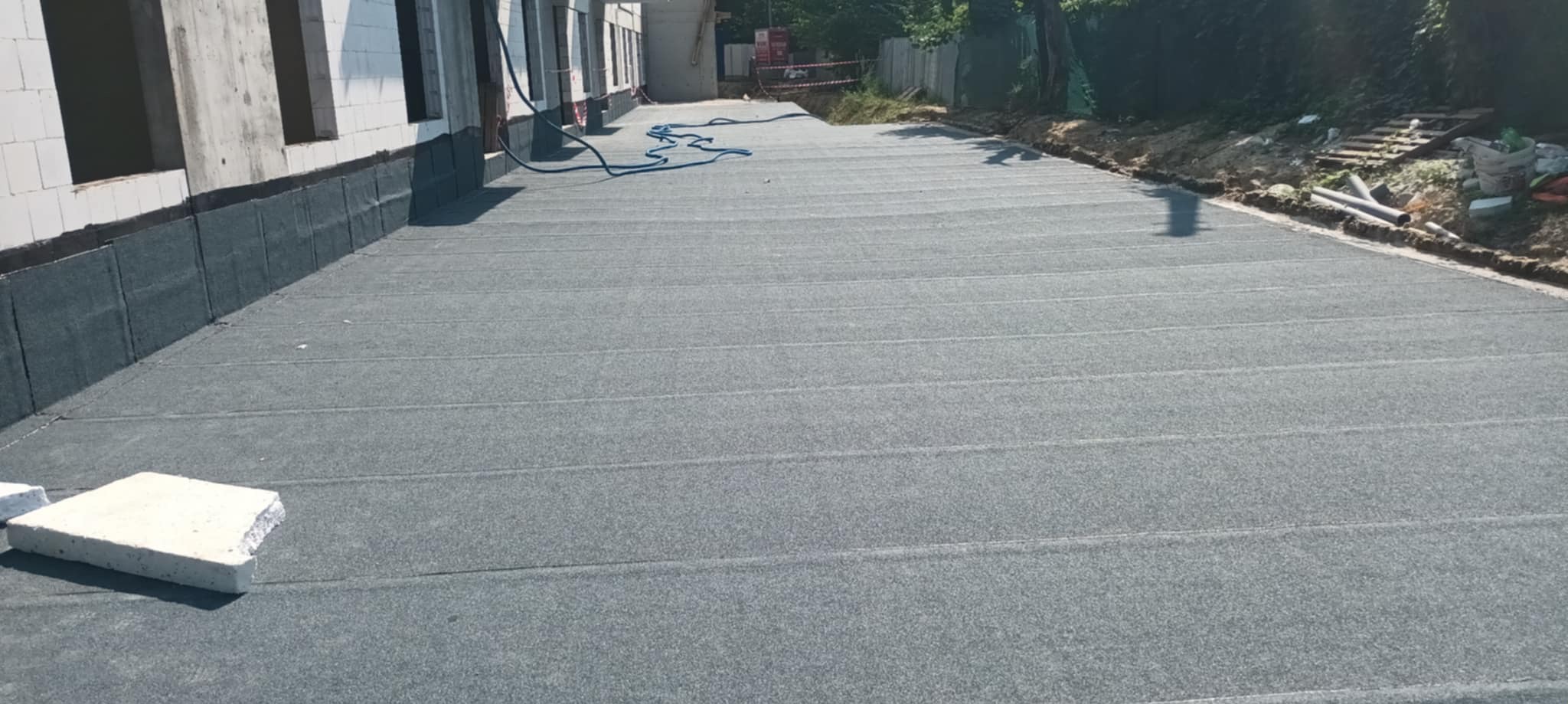 Szary, płaski dach pokryty papą termozgrzewalną na budynku w stanie surowym otwartym, z widocznymi fragmentami muru i instalacji.