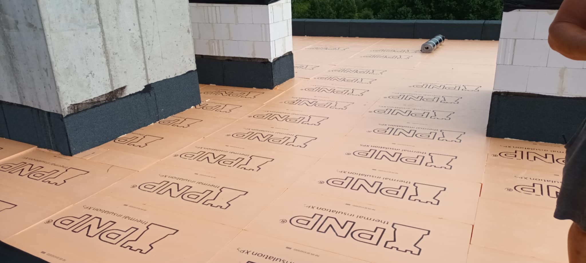 Izolacja termiczna XPS ułożona na dachu, widoczne bloczki betonowe z izolacją. Prace dekarskie w toku, przygotowanie do dalszych etapów.