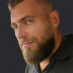 Portret brodatego mężczyzny z krótkimi włosami w szarej koszulce polo na ciemnym tle. Mężczyzna patrzy w lewo z lekkim uśmiechem.