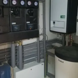 Zamknięta instalacja grzewcza z piecem gazowym Vaillant, czarnym panelem sterowania Afriso z manometrami i orurowaniem w szarej izolacji.