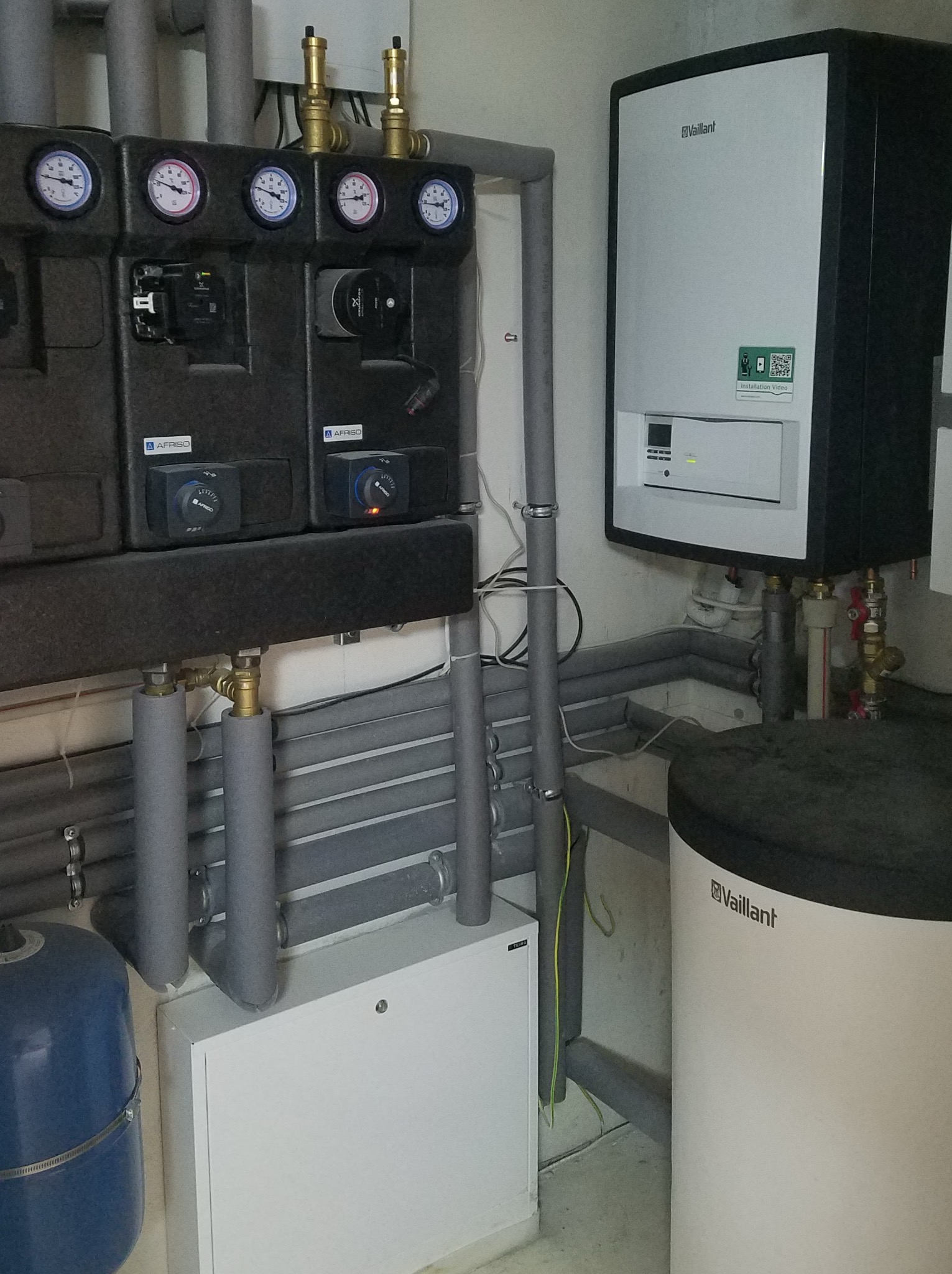 Zamknięta instalacja grzewcza z piecem gazowym Vaillant, czarnym panelem sterowania Afriso z manometrami i orurowaniem w szarej izolacji.