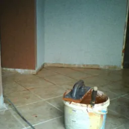 Ułożona podłoga z płytek w trakcie fugowania, widoczny kubeł z zaprawą, kielnia i fuga na płytkach.