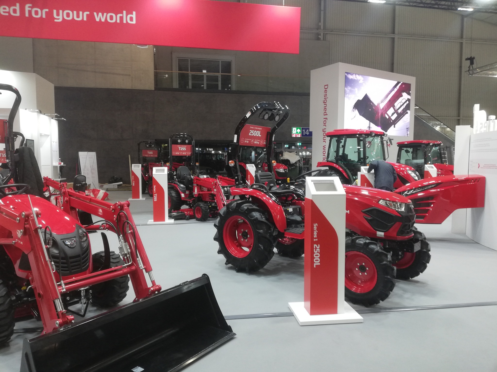 Czerwone traktory różnych modeli na wystawie, z widocznymi detalami konstrukcyjnymi i oznaczeniami serii, prezentowane w jasnym, przestronnym wnętrzu hali.